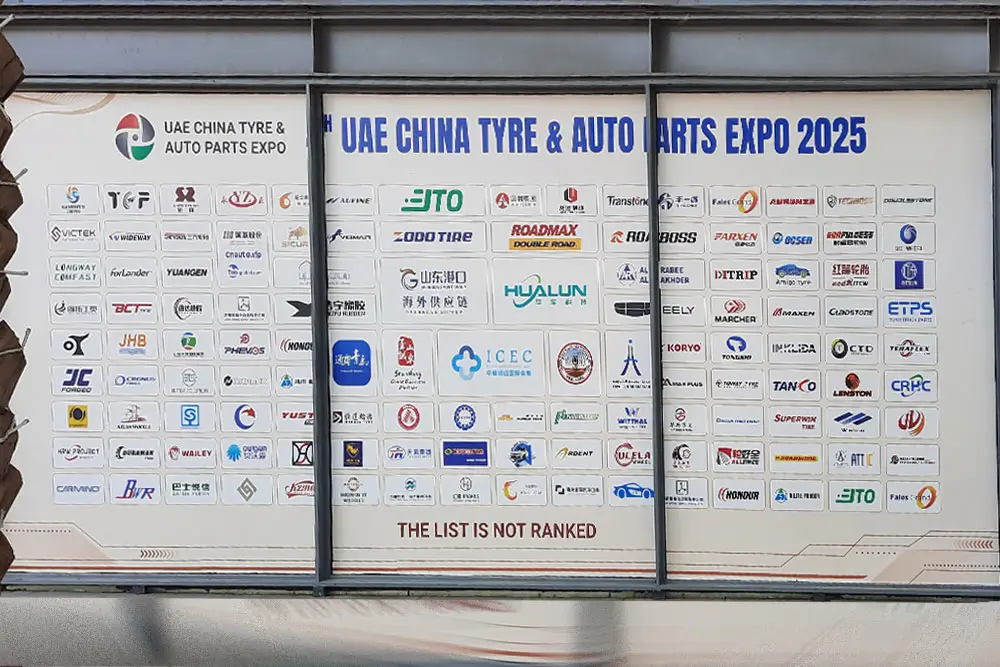 Wall of logos representing exhibitors at the UAE China Tyre & Auto Parts Expo 2025, including Fales Grand and other global automotive brands.